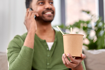 Image showing man with takeaway food calling on phone at home