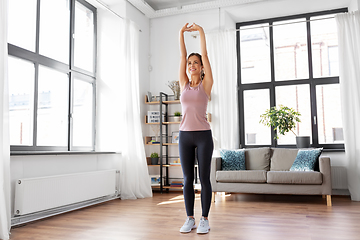 Image showing smiling young woman stretching arms at home