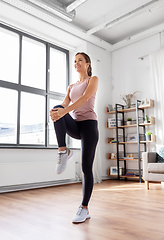 Image showing smiling young woman stretching leg at home