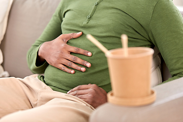 Image showing close up of overeaten man and cup of takeaway food