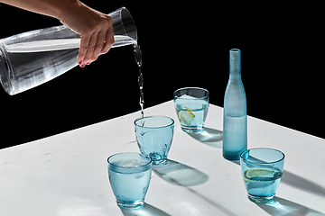 Image showing hand pouring water to glasses with lemon and ice