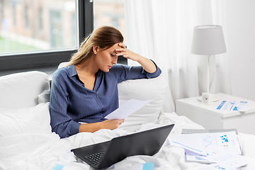 Image showing young woman with laptop and papers in bed at home