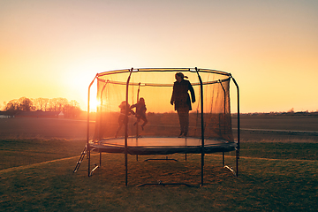 Image showing Trampoline on a lawn in the sunset with two kids