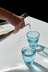 Image showing hand pouring water to glasses with lemon and ice