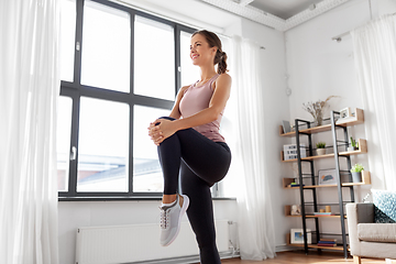 Image showing smiling young woman stretching leg at home