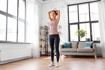 Image showing smiling young woman stretching arms at home