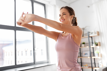 Image showing smiling young woman stretching arms at home