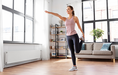 Image showing smiling young woman stretching leg at home