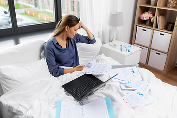 Image showing young woman with laptop and papers in bed at home