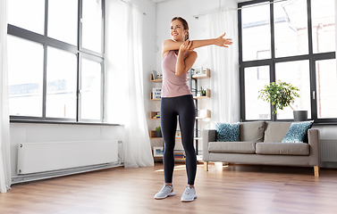 Image showing smiling young woman stretching arm at home