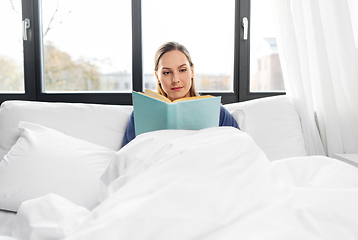 Image showing young woman reading book in bed at home