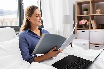 Image showing happy woman with laptop and folder in bed at home