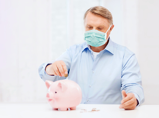 Image showing old man in mask putting coin into big piggy bank