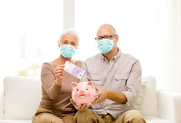 Image showing old couple in masks putting money into piggy bank