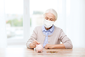 Image showing old woman in mask putting coin into piggy bank