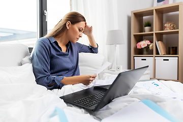 Image showing young woman with laptop and papers in bed at home