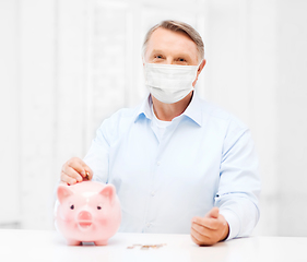 Image showing old man in mask putting coin into big piggy bank