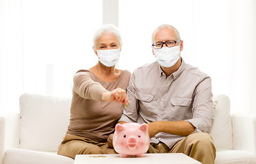 Image showing old couple in masks putting coin into piggy bank