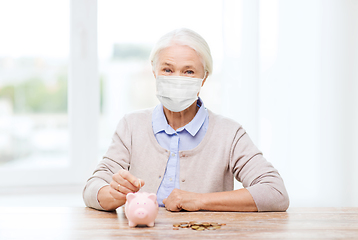 Image showing old woman in mask putting coin into piggy bank