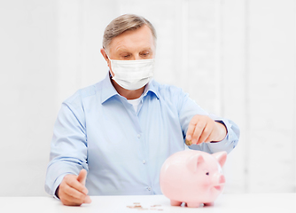 Image showing old man in mask putting coin into big piggy bank