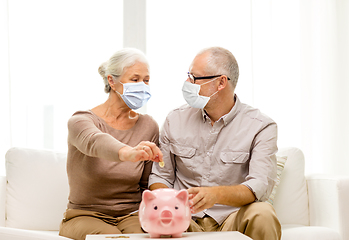 Image showing old couple in masks putting coin into piggy bank