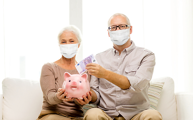 Image showing old couple in masks putting money into piggy bank