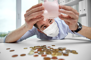 Image showing businessman in mask shaking piggy bank for money