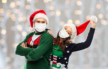 Image showing couple in masks, christmas sweaters and santa hats
