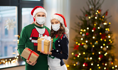 Image showing couple in masks, christmas sweaters with gifts