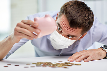 Image showing businessman in mask shaking piggy bank for money