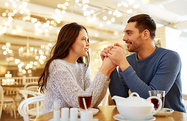 Image showing happy couple with tea holding hands at restaurant