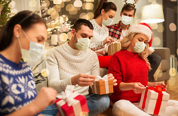 Image showing friends in masks opening christmas gifts at home