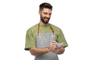 Image showing smiling waiter in apron taking notes to notepad