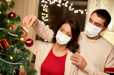 Image showing couple in masks decorating christmas tree at home