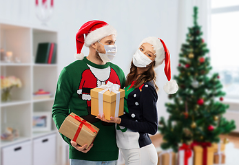 Image showing couple in masks, christmas sweaters with gifts