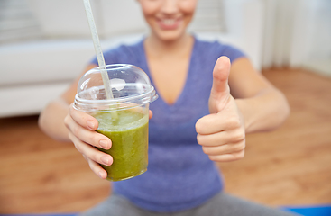 Image showing happy woman with cup of smoothie showing thumbs up