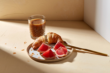 Image showing glass of coffee, croissant and grapefruit on table