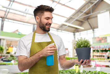 Image showing happy male gardener moisturizing flower at shop