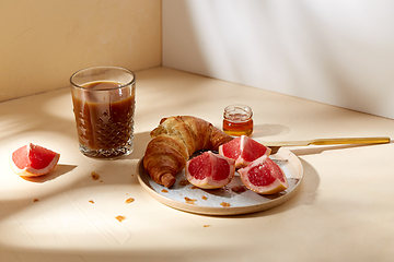 Image showing glass of coffee, croissant and grapefruit on table