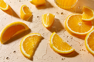 Image showing glass of juice and orange slices on wet table
