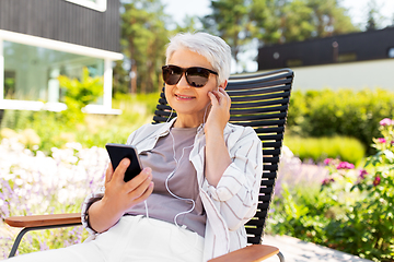 Image showing old woman with earphones and smartphone at garden