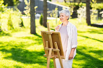 Image showing senior woman with easel drawing outdoors