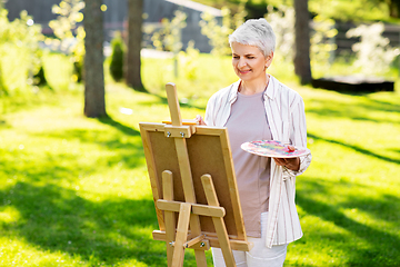 Image showing senior woman with easel painting outdoors