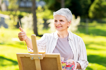 Image showing senior woman with easel painting outdoors