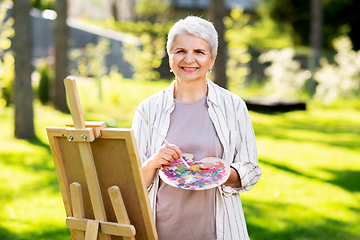 Image showing senior woman with easel painting outdoors