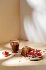 Image showing glass of coffee, croissant and grapefruit on table