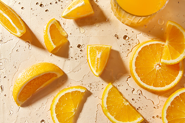 Image showing glass of juice and orange slices on wet table