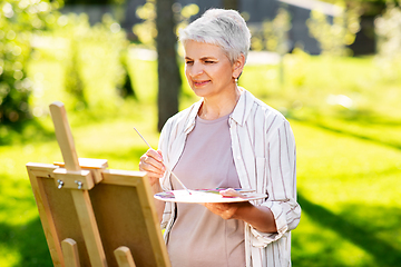 Image showing senior woman with easel painting outdoors