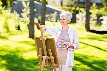 Image showing senior woman with easel painting outdoors