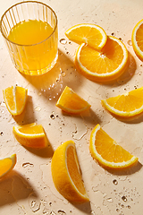 Image showing glass of juice and orange slices on wet table